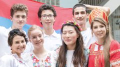 Seven college students of various heights, skin tones, and clothing colors pose smiling for a group photo in front of a blue and red background.